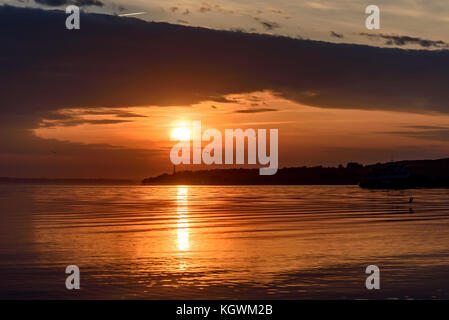 Sehr schönes, helles rot und orange Sonnenuntergang über dem Fluss mit Möwen über Wasser, Sonne und Wolken im Wasser widerspiegelt Stockfoto