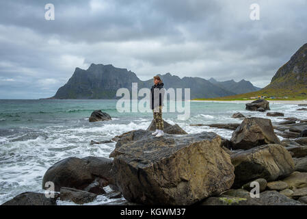 Boy steht auf einem großen Felsen und geniesst die Aussicht über einen Strand in Norwegen Stockfoto