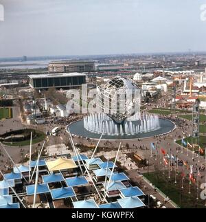 Panorama-Luftaufnahme nach Nord-Nordwesten, aufgenommen vom Aussichtsturm des New York State Pavilion auf der New York World's Fair, Flushing Meadows-Corona, Queens, New York, Mai 1965. Links im Vordergrund befindet sich der New Jersey Pavilion neben dem von Flaggen gesäumten Court of Nations. In der Mitte des Rahmens befindet sich die Stahlskulptur Unisphere und der Brunnen der Kontinente. Viele Besucher gehen durch den platz, und eine große Menschenmenge versammelt sich in der New England States Ausstellung in der Mitte links. Das Gebäude des United States Pavilion steht am Fuße des Court of States oben links. Direkt dahinter ist Shea Stadium. Stockfoto