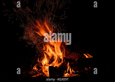 Rot und Orange Spurte der Flammen, Holzkohle, Brennholz im Feuer und Funken in Form von Tracks auf schwarzem Hintergrund Stockfoto