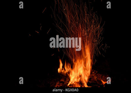 Rot und Orange Spurte der Flammen, Holzkohle, Brennholz im Feuer und Funken in Form von Tracks auf schwarzem Hintergrund Stockfoto