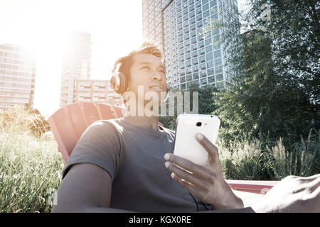 Trendy Kerl hören von Musik im Park, Long Island Stockfoto