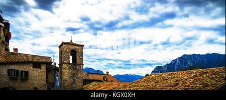 Blick über die Dächer auf einer kleinen Kirche in den Bergen am Gardasee unter einem stark bewölkten Himmel. Stockfoto