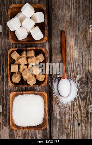 Drei Schalen mit Zucker und einem Löffel aus Holz auf einem alten Holz- Hintergrund, Ansicht von oben Stockfoto