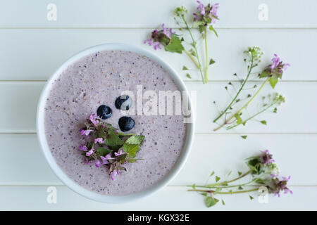 Haferflocken Porridge aus Hafer, zerdrückte Banane, Mandelmilch und Beeren, alle miteinander vermischt, auf weißem Holz- Hintergrund mit frischem Thymian und sh isoliert Stockfoto