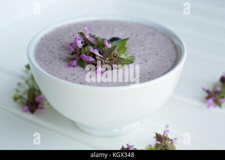 Haferflocken Porridge aus Hafer, zerdrückte Banane, Mandelmilch und Beeren, alle miteinander vermischt, auf weißem Holz- Hintergrund mit frischem Thymian und sh isoliert Stockfoto