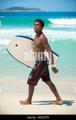 RIO DE JANEIRO - 6. FEBRUAR 2017: Junger brasilianischer Surfer spaziert mit seinem Bodyboard am Strand von Arpoador entlang, der beliebten Surfpause. Stockfoto