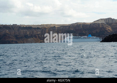 Kreuzfahrtschiff vor der Küste von Santorini an einem bewölkten Tag. Stockfoto