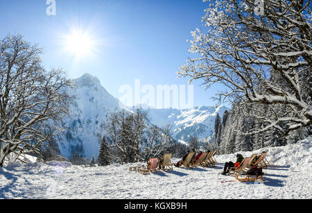 Gruppe von Menschen sitzen mit Liegestühlen im Winter Berge. Sonnenbaden im Schnee. Deutschland, Bayern, Allgäu, schwarzenberghuette. Stockfoto