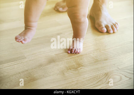 Baby und Mutter Füße sind zu Fuß auf dem hölzernen Fuss. Traum unscharf. Stockfoto