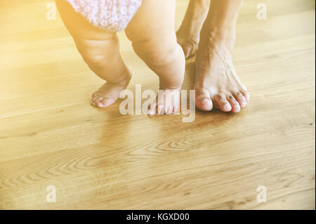 Baby und Mutter Füße sind zu Fuß auf dem hölzernen Fuss. Traum unscharf. Stockfoto