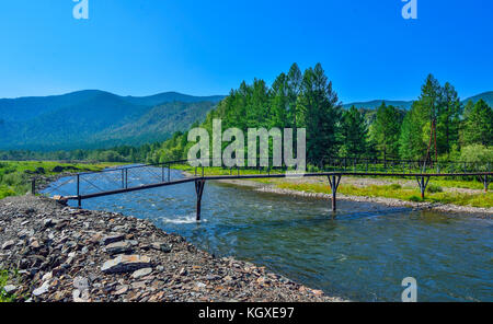 Helle Sommer Landschaft mit leicht metallischen Brücke über schnelle mountain river mit steinigen Ufer fließenden unter den grünen Wald, Altai Gebirge, Russland Stockfoto