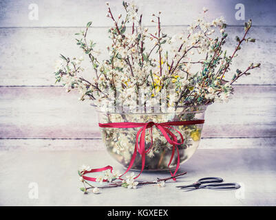 Frühling Cherry Blossom Zweige Strauß in der Vase mit Band- und Scherkräfte auf rustikalen Tisch an der hölzernen Wand Hintergrund Stockfoto