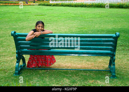Mädchen sporting Lächeln zurück sitzt auf einem grünen Garten Bank Stockfoto