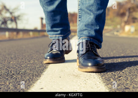 Frau füsse treten auf der Mitte der Straße mit schwarzen Leder Schuhe und Jeans an einem sonnigen Tag im Herbst oder fallen Stockfoto