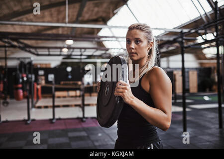 Junge blonde Frau in der Turnhalle clohting Tragen Gewichte für ein Training Session, während allein in der Turnhalle stehen Stockfoto