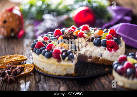 Käsekuchen mit frischen Obstbeeren Erdbeeren Himbeeren und Sternanis. Weihnachtsstimmung mit weihnachtsdekoration. Stockfoto