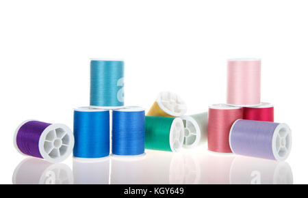 Viele Spulen des Nähgarne gestapelt und auf der Seite isoliert auf Weiss auf einer reflektierenden Oberfläche zufällig zur Festlegung und gestapelt Stockfoto