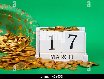 Bis auf Holzblöcke mit Datum 17. März 2010 in der Nähe der Saint Patrick's Day, sitzend auf grünem Hintergrund, Kobold hut mit Goldmünzen verschütten ou Stockfoto
