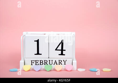 Holz Block mit Kalender Datum 14. Februar, Valentinstag, sitzend auf rosa Hintergrund mit Süßigkeiten Herzen vor gesäumt. Stockfoto