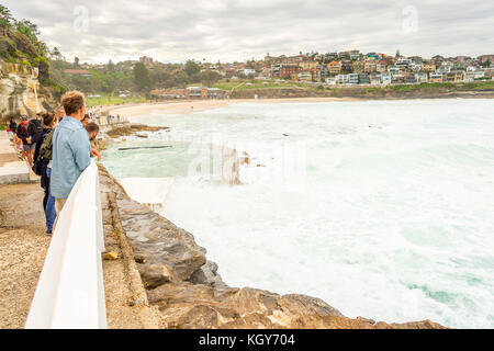 Touristen und Einheimische Surfer beobachten, wie das Wasser aus dem Felsen pool Bronte Beach in Sydney, NSW, Australien in Big Surf eingeben Stockfoto