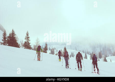 Gruppe von zurück Langläufer gehen durch einen nebligen Tal. Stockfoto