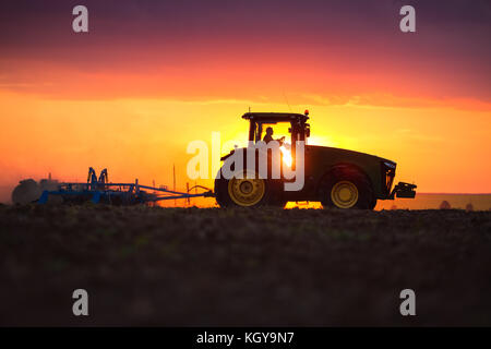 Bauer im Traktor Vorbereitung land mit saatbeet Kultivator, Sonnenuntergang geschossen Stockfoto