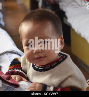 Kleiner, süßer kasachischer Junge mit Asiaten mit schwanzäugigen Augen, der jemanden anstarrt, der lächelnd einen Winterpullover trägt. Stockfoto