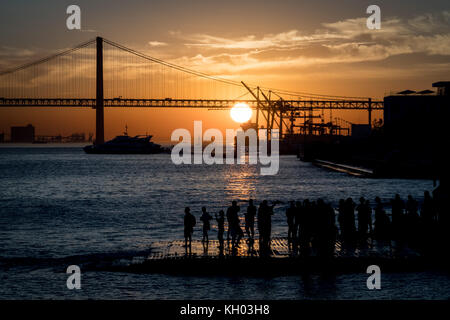 Lissabon, Portugal, 27. Oktober 2017 Menschen den Sonnenuntergang mit Blick auf "25 de Abril" Brücke über den Fluss Tejo in der Nähe von Praça do Comercio in Lissabon, Portug Stockfoto