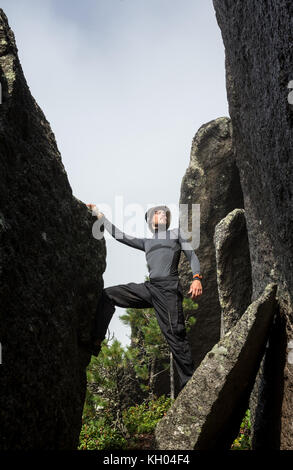 Männliche Kletterer. Kletterer auf einem schwarzen felsige Wand auf dem Ozean Bank in Island klettert, kirkjufjara Strand. Man macht kaum bewegen, ohne Seil. Stockfoto