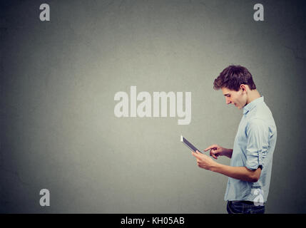 Schöner Mann im blauen Hemd ist mit einem digitalen Tablet und lächelnd auf grauen Hintergrund isoliert Stockfoto