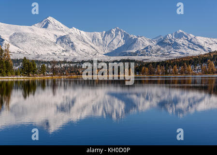 Helle malerischen Herbst Ansicht mit einem wunderschönen See, Wald, schneebedeckte Berge und ihre Überlegungen auf dem Hintergrund der blauen Himmel an einem sonnigen Tag Stockfoto