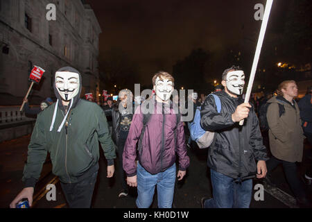 Demonstranten tragen Guy Fawkes Masken und halten selbstgemachte Schilder und Plakate mit politischen Botschaften auf der Million Mask March 2015 in London hoch. Stockfoto