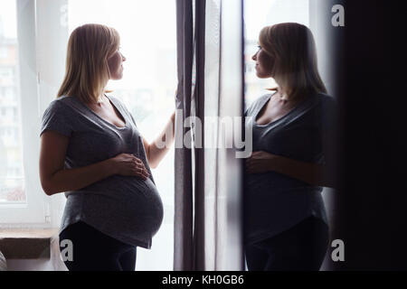 Schwangere Frau Silhouette, die man vom Fenster aus sieht, in einer Glasscheibe reflektiert. Stockfoto