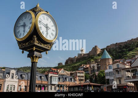 Tiflis, Georgien, Osteuropa - die prunkvolle öffentliche Uhr im Stadtteil Altstadt mit der Festung Narikala dahinter. Stockfoto