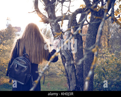 Das Mädchen steht mit dem Rücken zugewandt. Sie in die Ferne sieht. Um voller Laub. Stockfoto