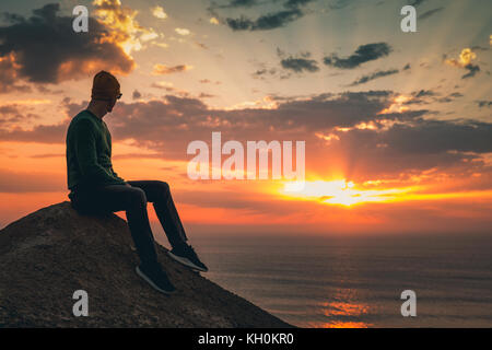 Junger Mann sitzen und den wunderschönen Sonnenuntergang beobachten Stockfoto