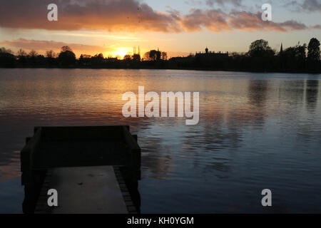 Lurgan Park See, Nordirland, Großbritannien. 12. November 2017. Ein blustery Tag mit kalten Nord-westlichen Winden und Duschen endet mit Clearing Skies und fallende Temperaturen. Frost zu rechnen ist, möglicherweise als niedrig zu-4C in ländlichen Gebieten, wie die Sonne auf der linken Seite von Shankill Pfarrkirche und Brownlow House (rechts). Quelle: David Hunter/Alamy Leben Nachrichten. Stockfoto