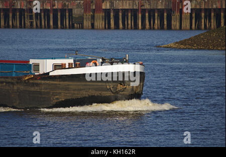 Der Bogen der Binnenschiff mit voller Geschwindigkeit mit weiß schäumenden Bugwelle und Pier im Hintergrund Stockfoto