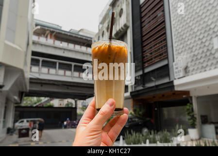 Eine menschliche Hand mit einem frisch zubereiteten Glas thai Eiskaffee in Bangkok Seitenstraße. Stockfoto