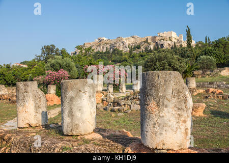 Reste von Gebäuden im alten Athen "Agora, blühenden Bäumen und die Senkrechte hänge von der Akropolis im Hintergrund Stockfoto