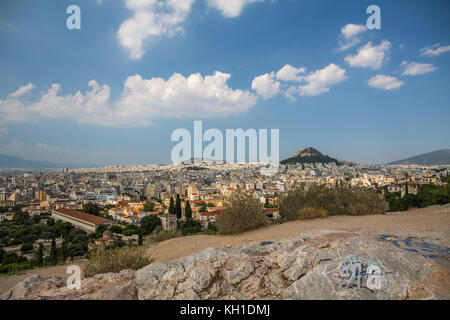 Die Stadt Athen breitet sich unterhalb des Marshügels aus, wo Felsen im Vordergrund von Grafitti geschmückt wurden. Hellweiße Wolken schweben im azurblauen blau Stockfoto