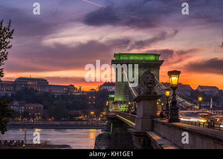 Budapest, Ungarn - Schöner goldener Sonnenuntergang an der Szechenyi-Kettenbrücke in grünen Lichtern mit Buda-Schloss-Königspalast im Hintergrund Stockfoto