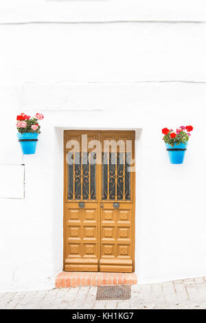 Hölzerne Tür gelb lackiert mit zwei blauen Töpfen hängen von der Wand auf beiden Seiten der Tür mit roten Geranien auf einer weißen Wand in Andalusien, Spanien, Stockfoto