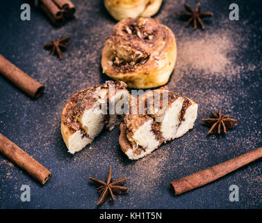 Brötchen mit Zimt und Nüsse auf schwarzem Hintergrund, Backpulver bestreut mit Zimt Stockfoto