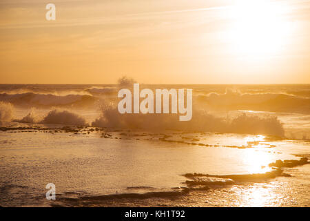 Große Wellen schlagen die Felsen, wie die goldene Sonne an der Küste von Heu el Fath, Rabat, Marokko. Stockfoto