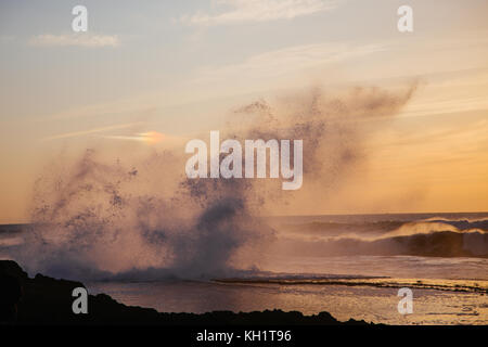 Große Wellen schlagen die Felsen, wie die goldene Sonne an der Küste von Heu el Fath, Rabat, Marokko. Stockfoto