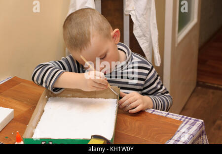 Junge im gestreiften Hemd am Tisch sitzen und basteln Stockfoto