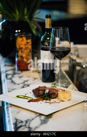 Ein Lammhackgericht mit einer Flasche und einem Glas Rotwein auf einer Marmorfläche Stockfoto