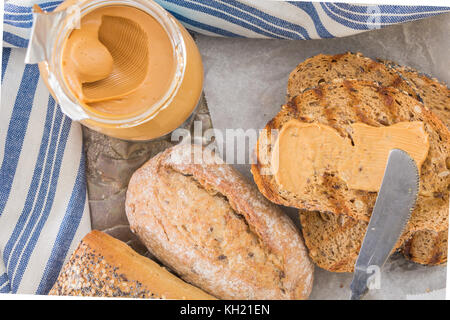 Vollkornbrot gegrillte Brotscheiben, mit geöffnetem Glas Erdnussbutter und Messer. Stockfoto